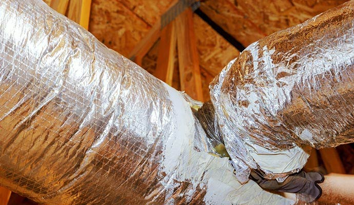 A technician is sealing a duct in an attic