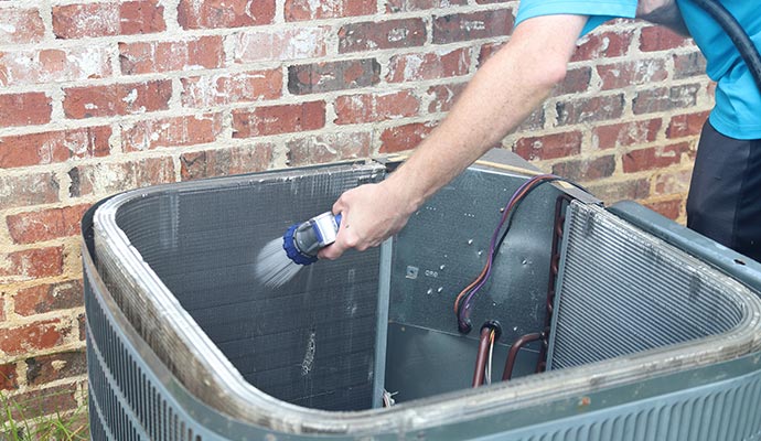 A technician is cleaning the air handler with a hose pipe.