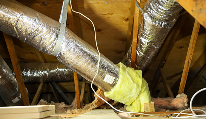 Silver flexible air ducts and yellow insulation installed in a home's attic space