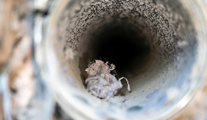 An interior view of a circular air vent almost entirely blocked by thick lint and dust buildup