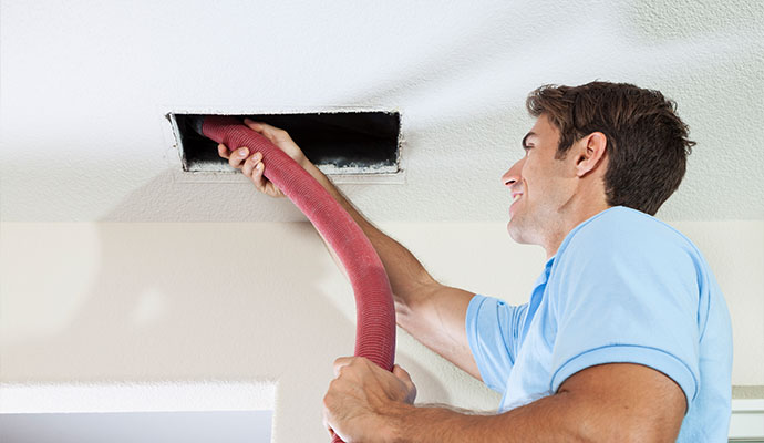 Technician vacuuming ceiling air duct