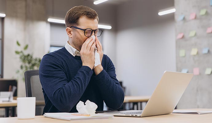 Man sneezing into a tissue at his office desk