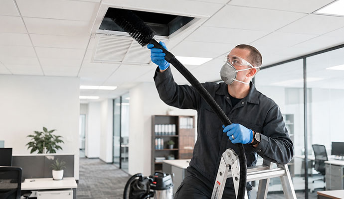 Technician cleaning a ceiling air duct in an office.